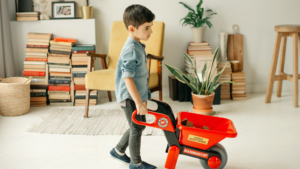 Niño pequeño con un carro de jugete rojo recogiendo los juguetes en el salón de su casa